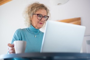 senior woman looking at laptop with mug