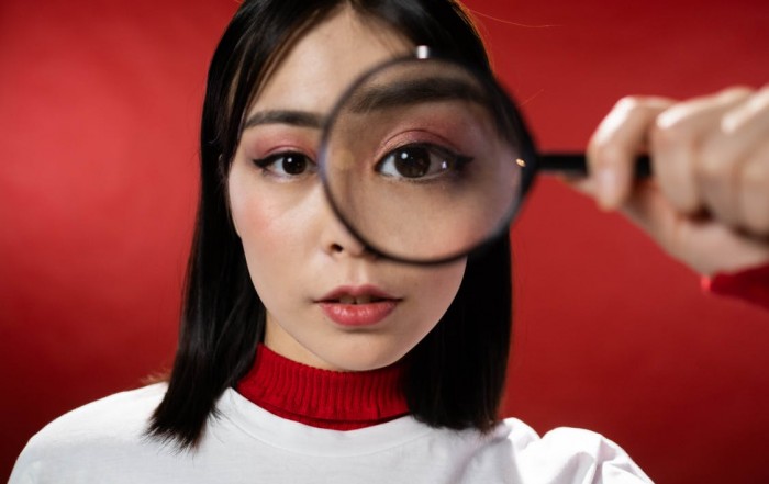 woman looking through magnifying glass with red background