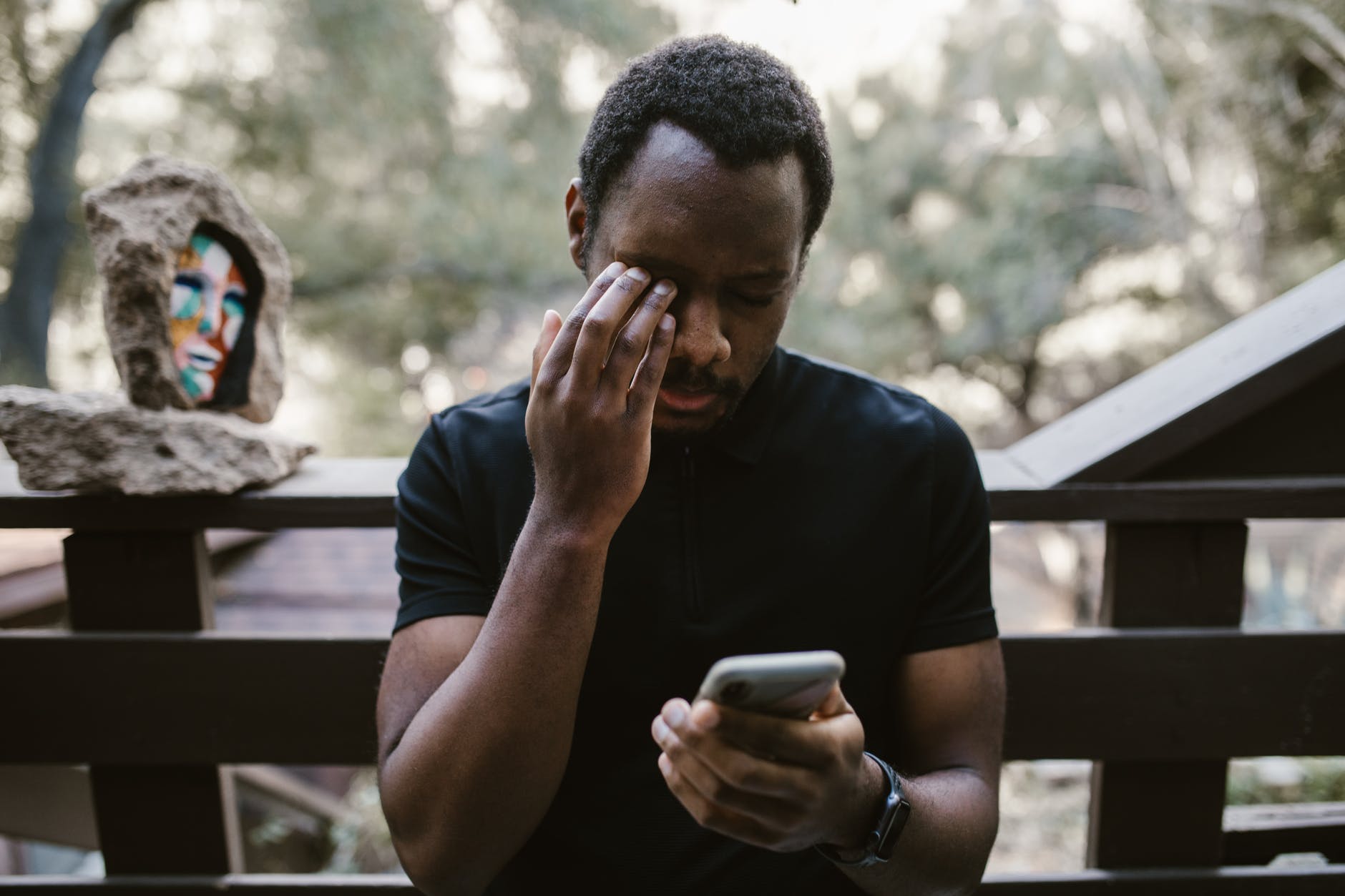 man wiping eye and holding cellphone