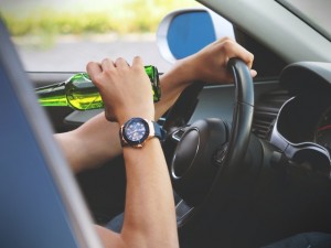 person drinking with hand on car steering wheel