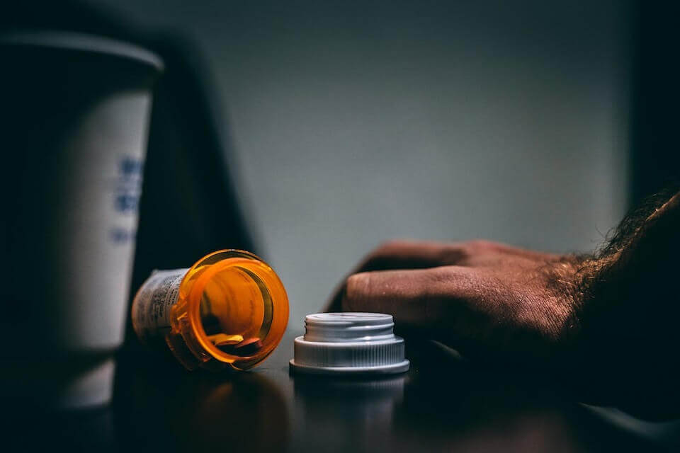 open bottle of prescription drugs next to person’s hand