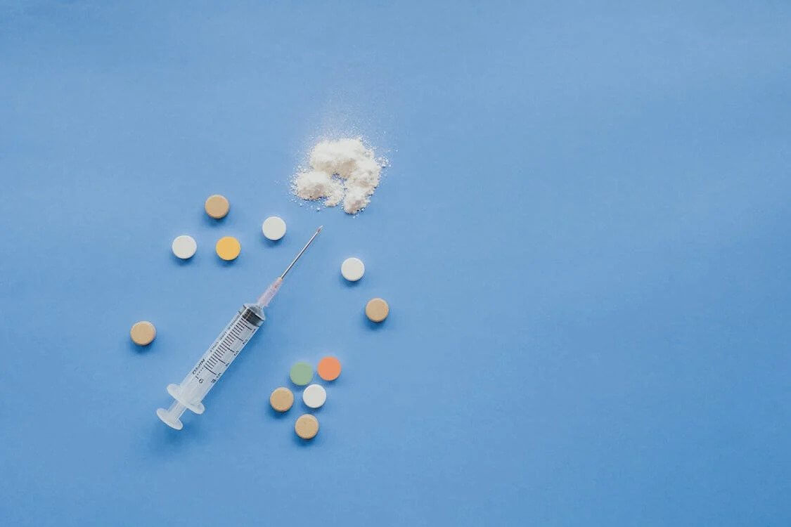 a syringe, pills and a pile of powder on a blue background