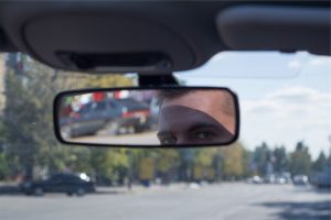 man looking in rearview mirror of his car