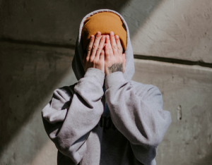 person in grey hoodie covering face with hands