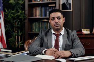 lawyer in grey suit sitting at a desk in front of documents