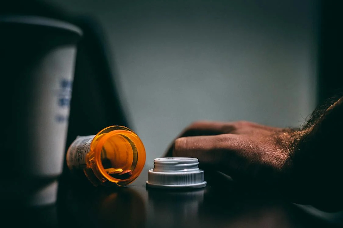 prescription bottle with cap off resting on its side next to a person's hand