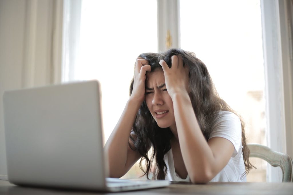 woman holding her head in frustration in front of laptop
