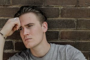 pensive man leaning against brick wall
