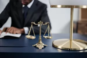 legal concept image - anonymous lawyer signing document in background, scale and lamp in foreground