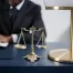 legal concept image - anonymous lawyer signing document in background, scale and lamp in foreground