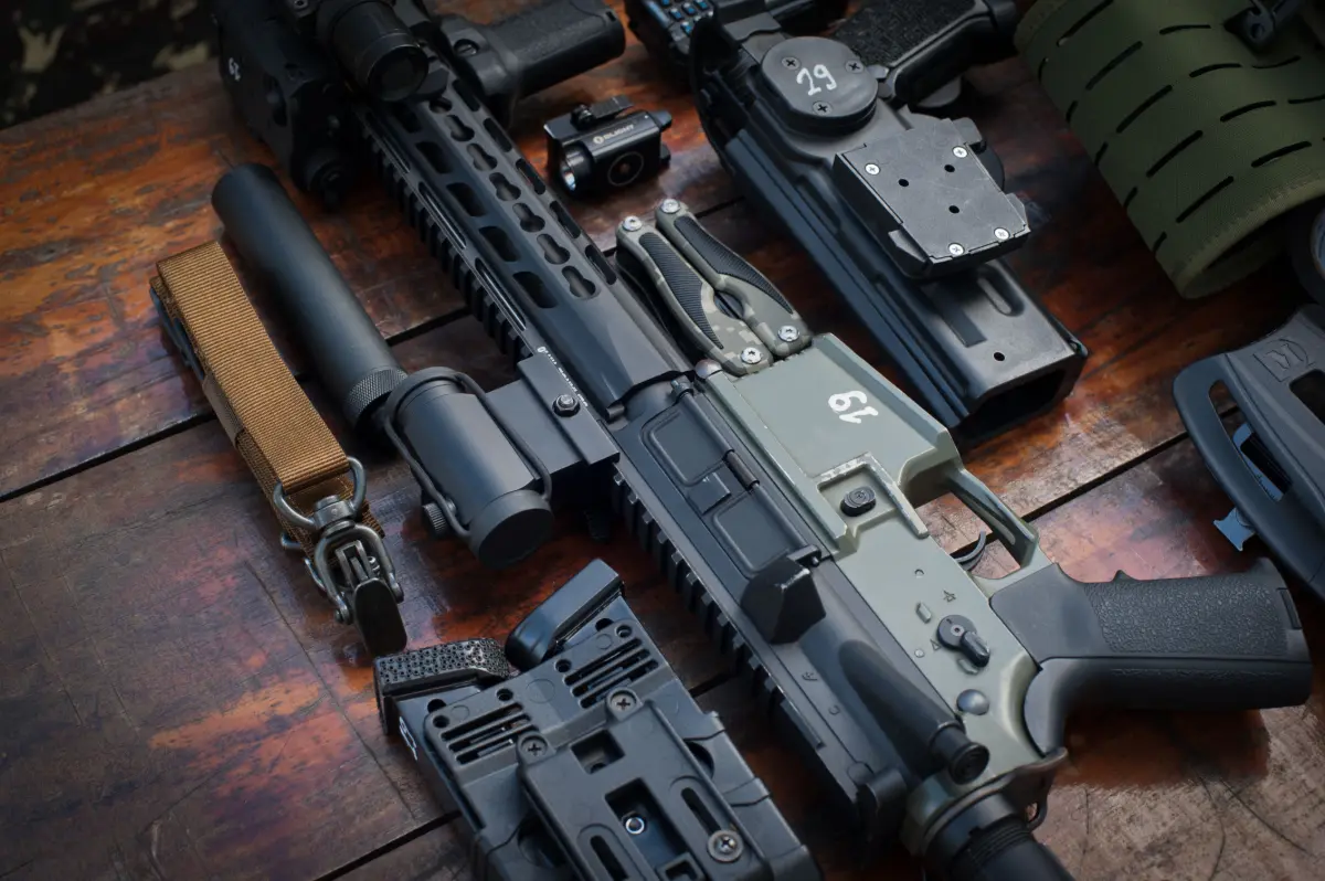 Close-up of tactical firearms and gear arranged on a rustic wooden surface