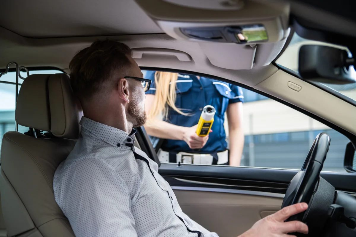 Police officer holding a breathalyzer at the window of a driver seated in his car